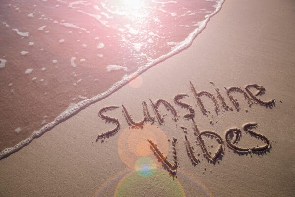 Sunshine Vibes tropical vacation message handwritten on a smooth sand beach with incoming wave
