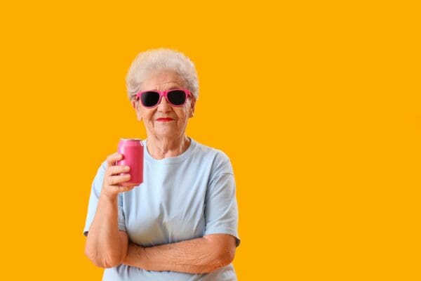 Senior woman in sunglasses with can of soda on yellow background
